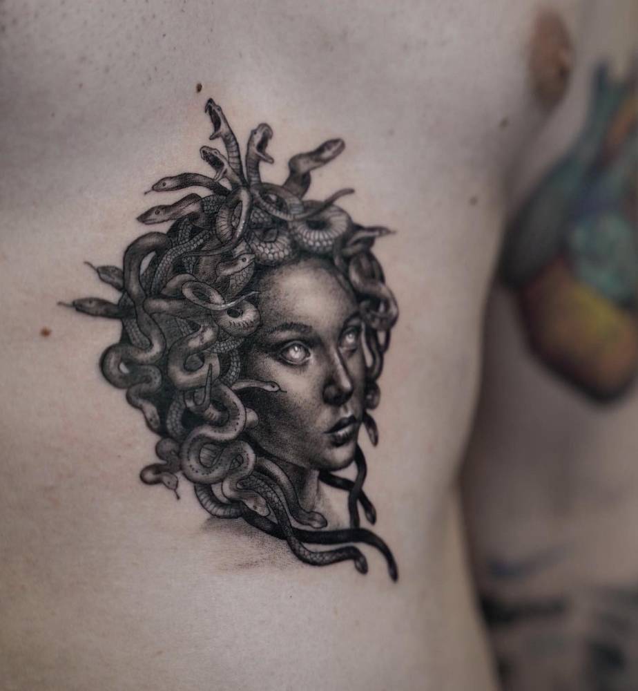 Medusa portrait in black and grey style located on the stomach.