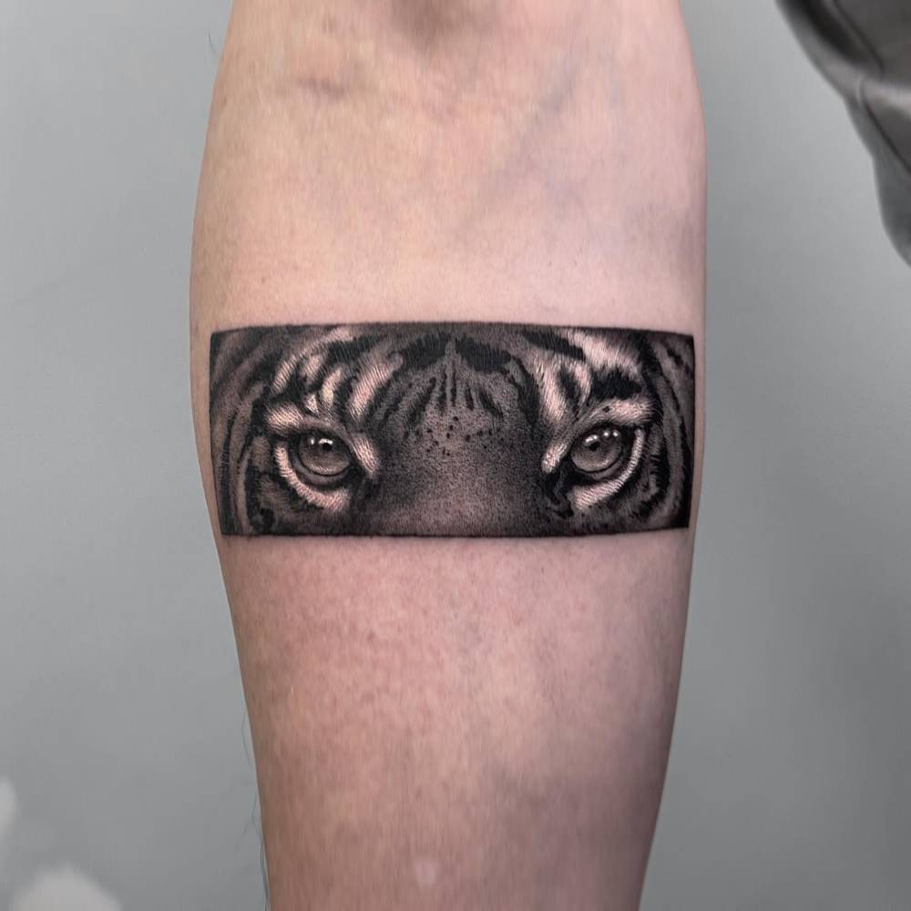 Tiger eyes tattoo in black and grey style located on the inner forearm.
