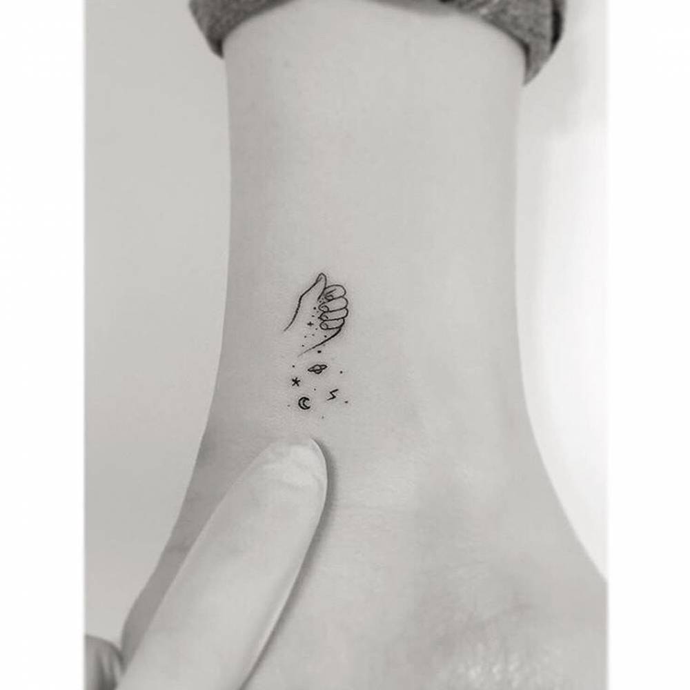 Minimalistic style hand holding a galaxy tattoo located on the ankle.