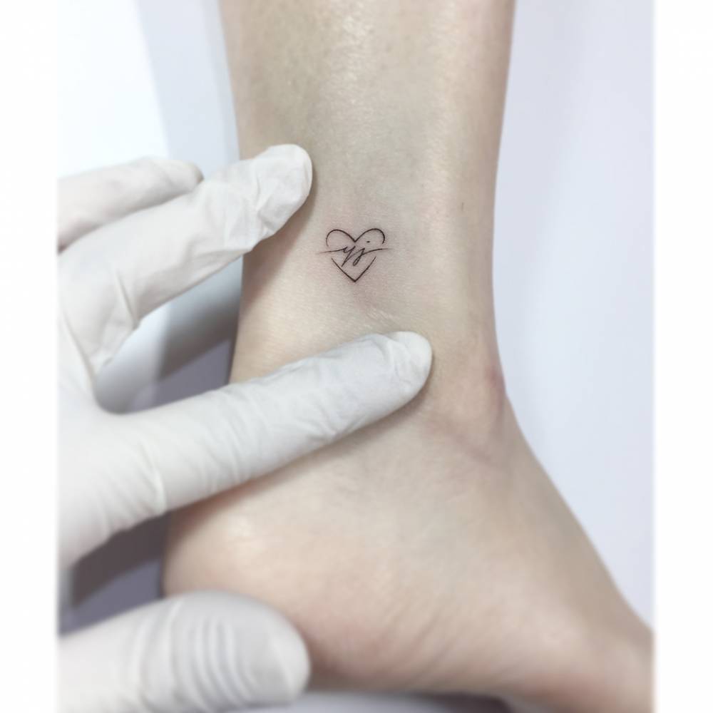 Heart and initials tattoo in minimalistic style placed on the ankle.