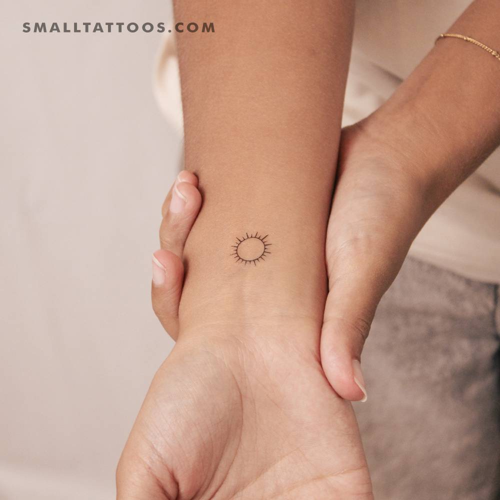 Small shining sun temporary tattoo located on the wrist.