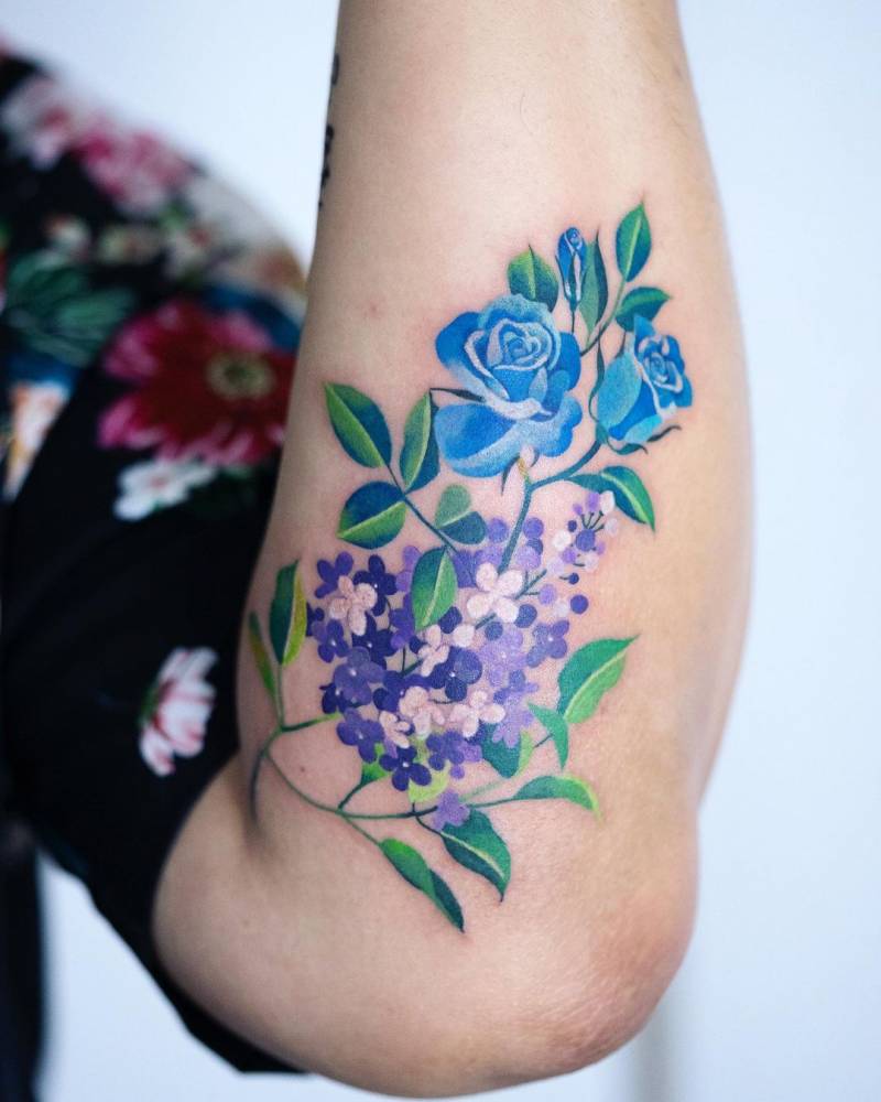 Lilac and blue rose tattoo located on the forearm.