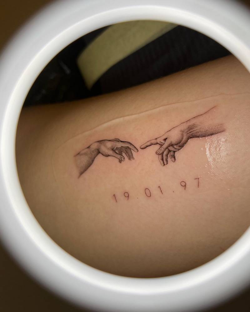 'The Creation of Adam' hands tattooed on the inner arm.