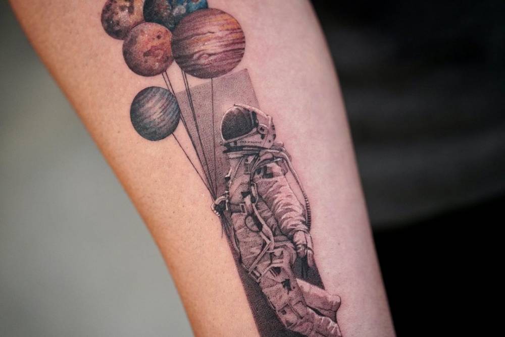 Micro-realistic astronaut and planets tattoo on the inner forearm.