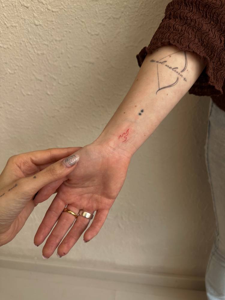 Minimalistic style red fire tattoo placed on the wrist.
