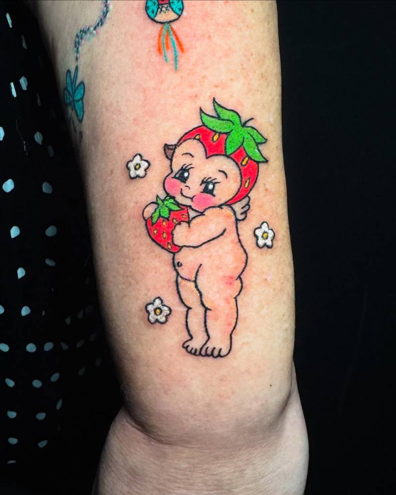 Strawberry kewpie tattoo located on the wrist, cartoon style.