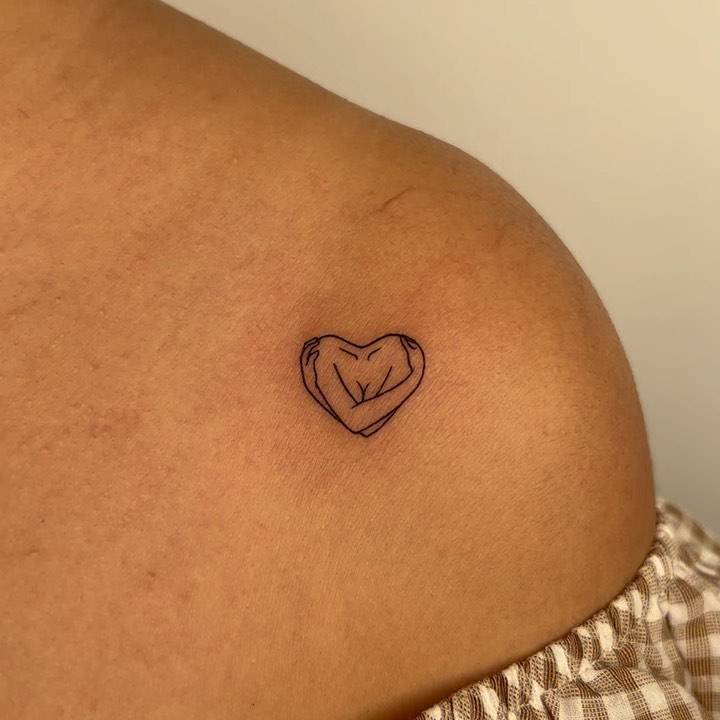 Minimalistic self hug tattoo placed on the shoulder.