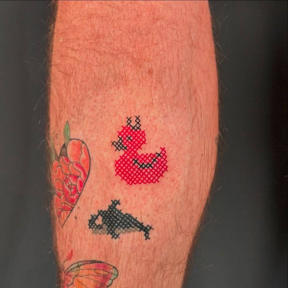 Devil duck tattoo in cross stitch style located on the calf.