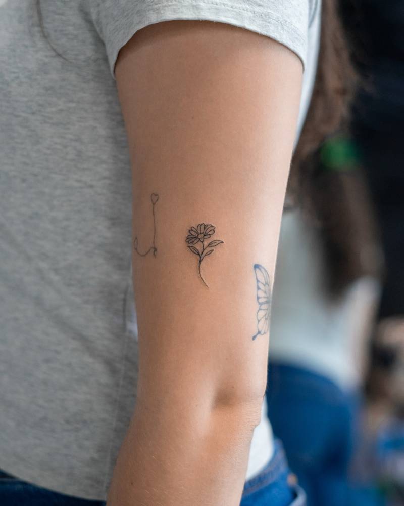Minimalistic style daisy flower tattoo located on the upper arm.