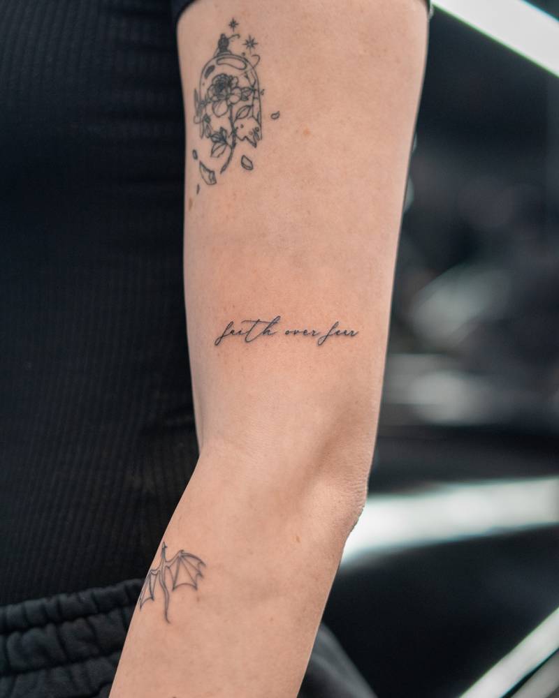 "Faith over fear" lettering tattoo handwritten on the upper arm.
