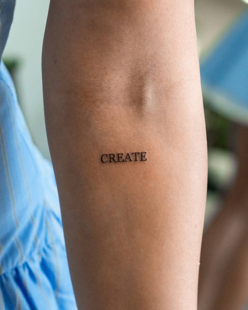 Serif font word "create" tattooed on the inner forearm.