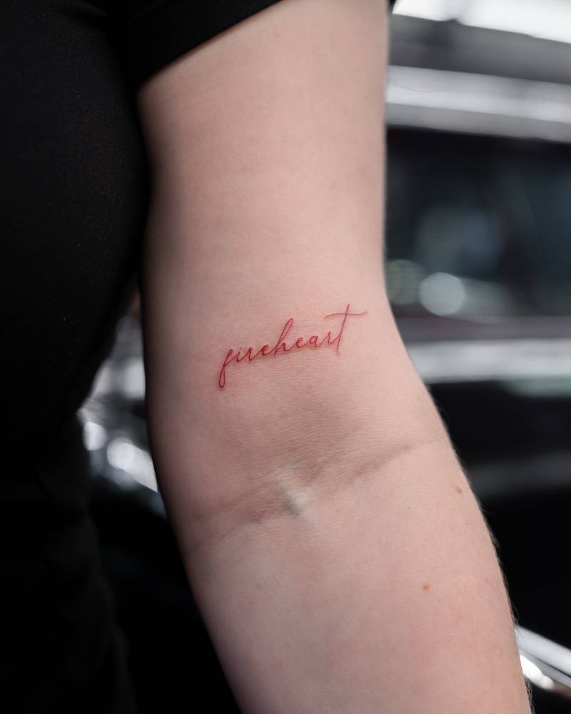Handwritten font word "fireheart" tattooed on the bicep.