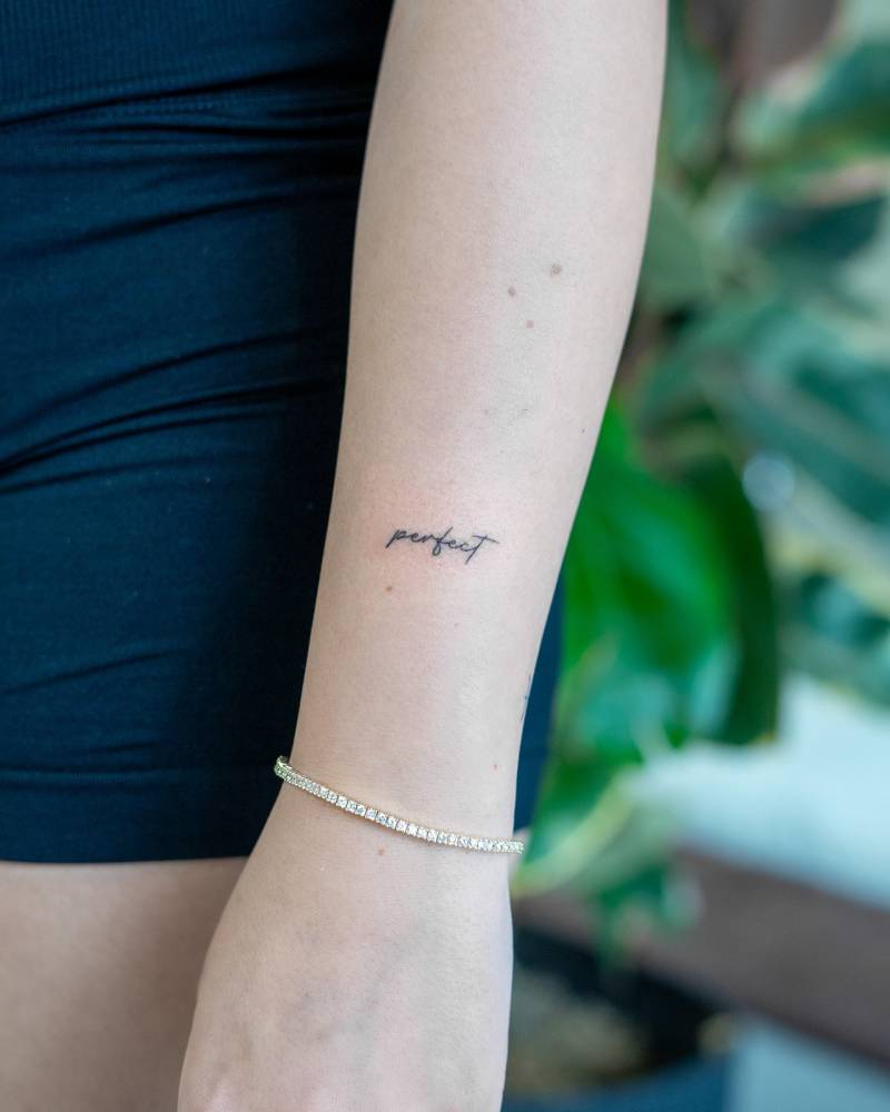 Handwritten font word "perfect" tattoo placed on the wrist.
