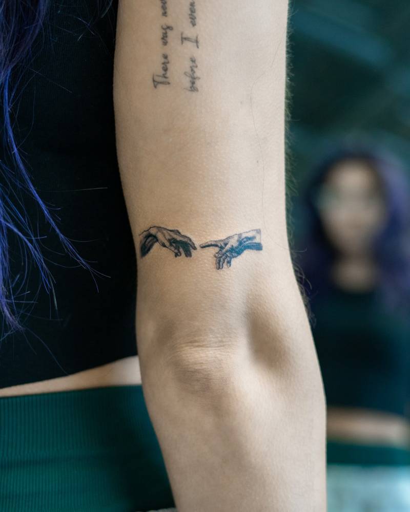 Illustrative style "The Creation of Adam' hands tattooed on the tricep.