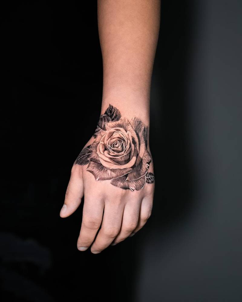 Black and grey rose head tattoo located on the hand.