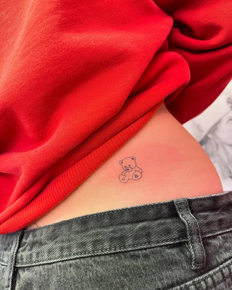 Fine line style teddy bear tattoo located on the lower back.