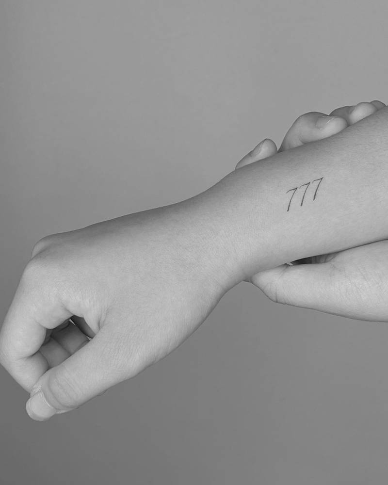 Angel number "777" tattoo located on the wrist.