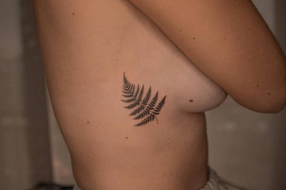 Micro-realistic style fern leaf tattoo located on the side boob.