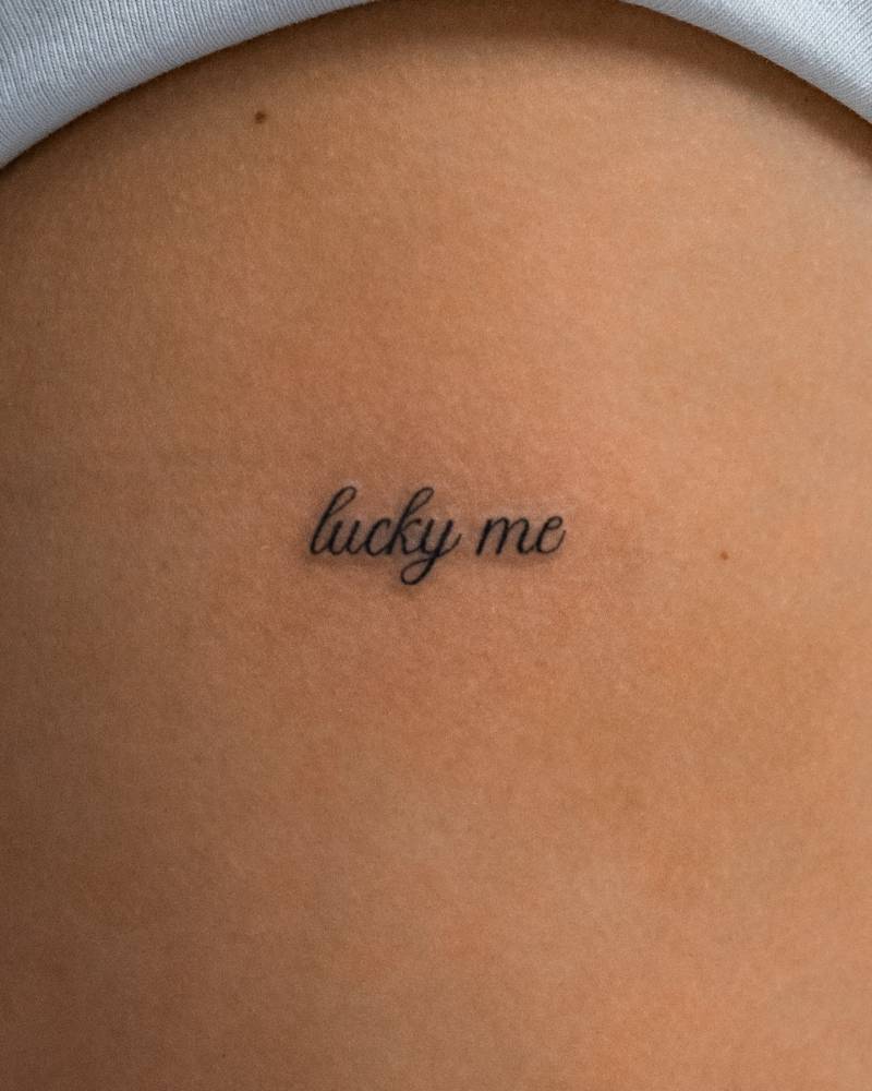 "Lucky me" lettering tattoo placed on the upper arm.