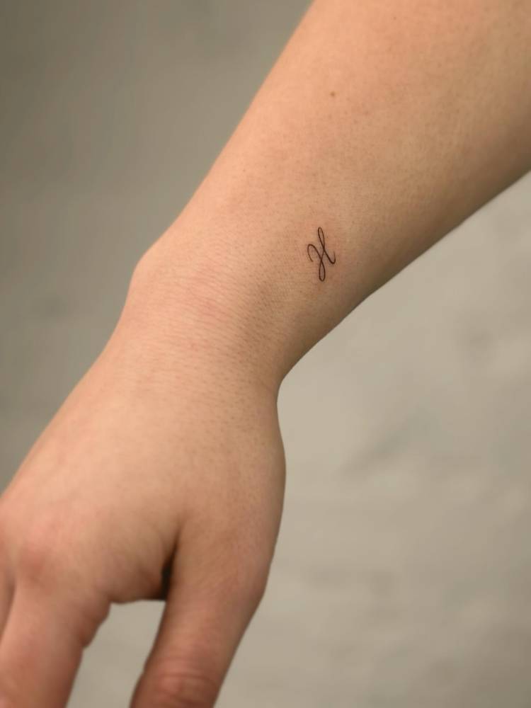 Tiny letter "H" tattoo in handwritten font placed on the wrist.