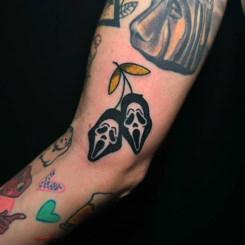Ghostface cherries tattooed on the inner arm, cartoon style.