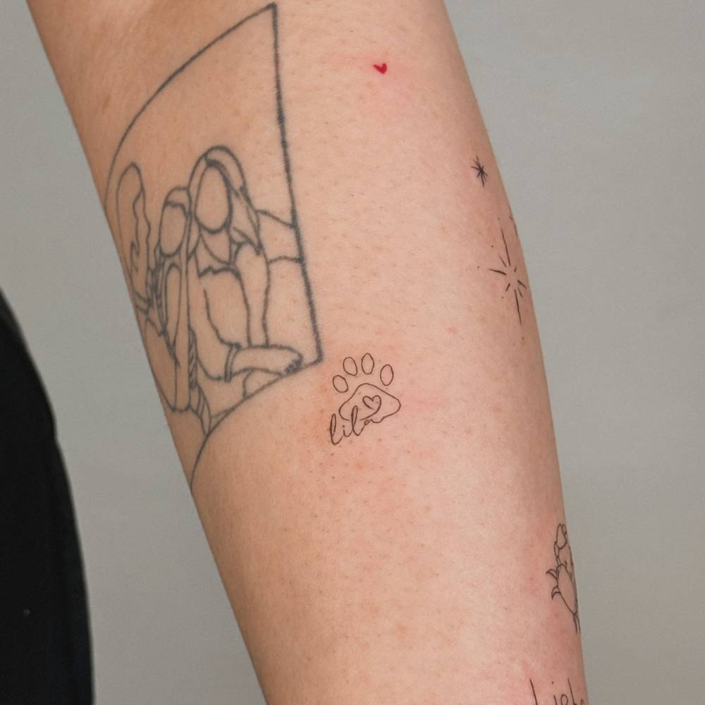 Paw print and name "Lila" tattooed on the forearm, fine line style.
