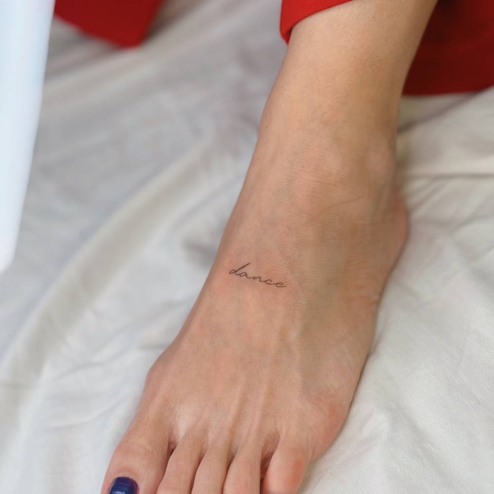 "Dance" lettering tattoo in handwritten font located on the foot.