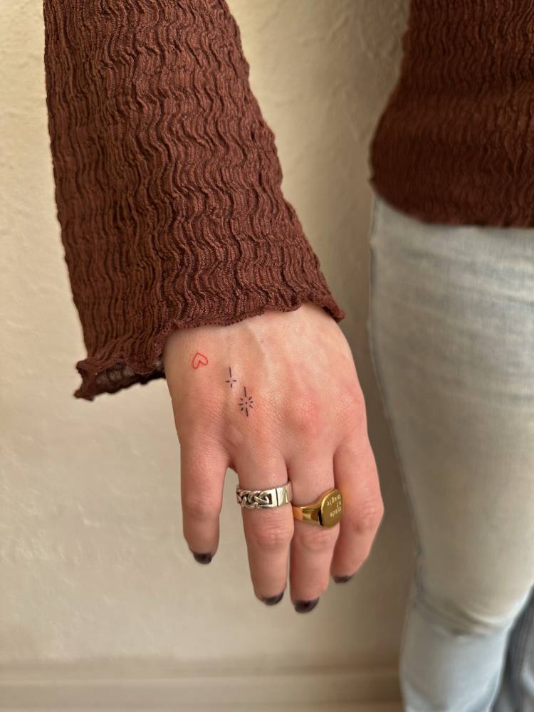 Sparkling stars and red heart tattoo located on the hand.