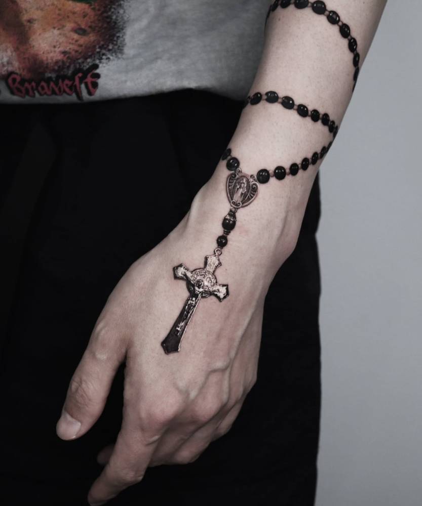 Black and grey rosary tattoo located on the wrist and hand.