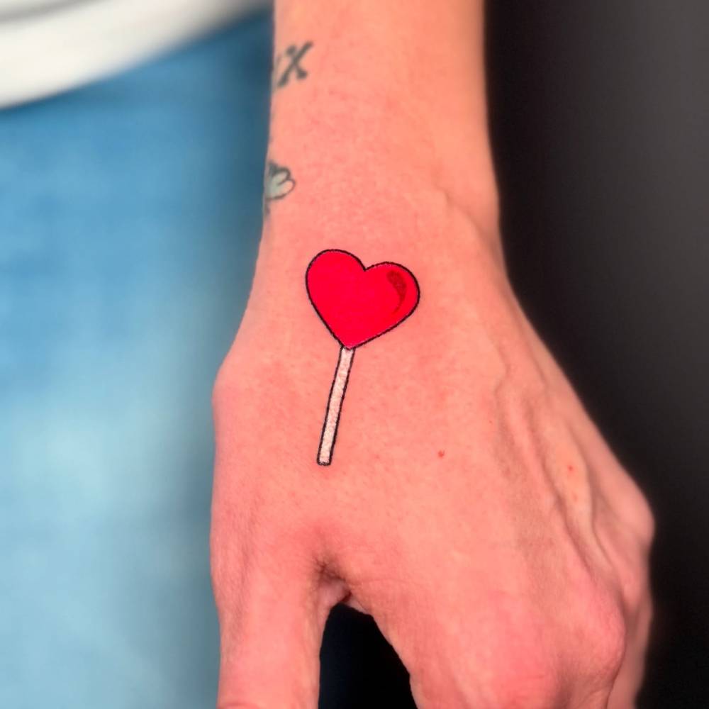 Heart lolly tattoo located on the hand.