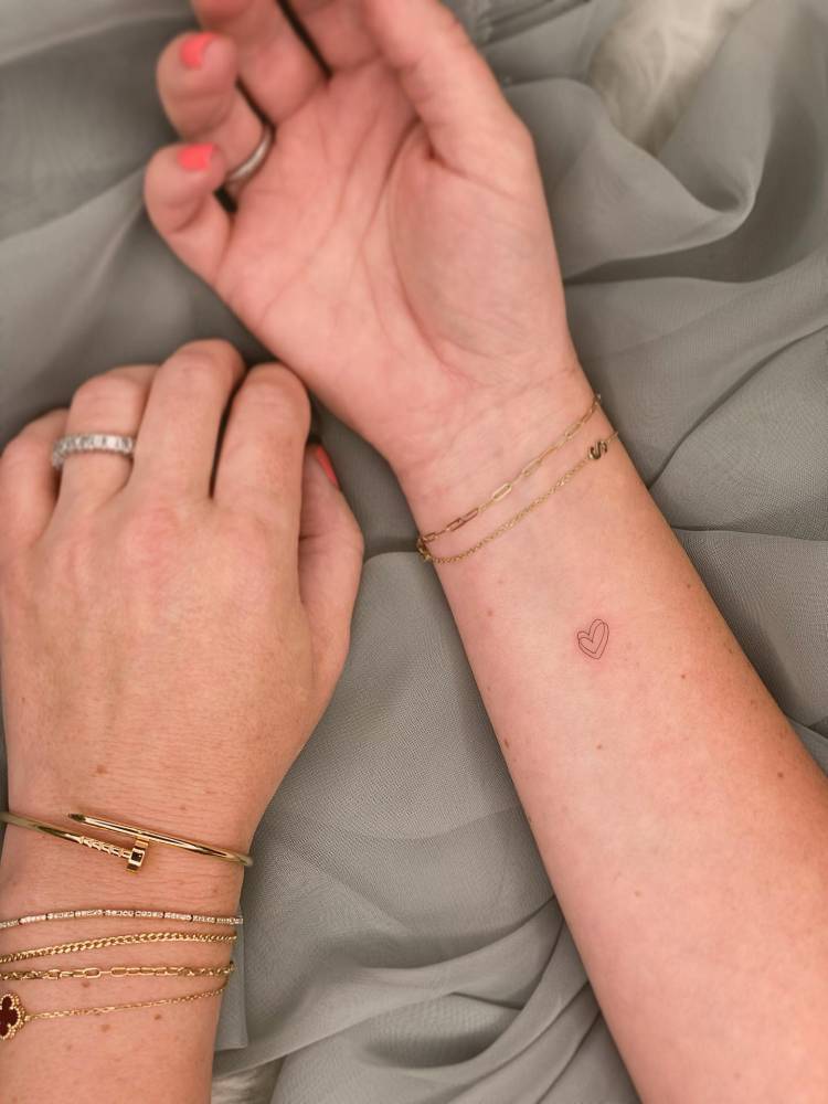 Tiny minimalistic heart tattoo in fine line style located on the wrist.