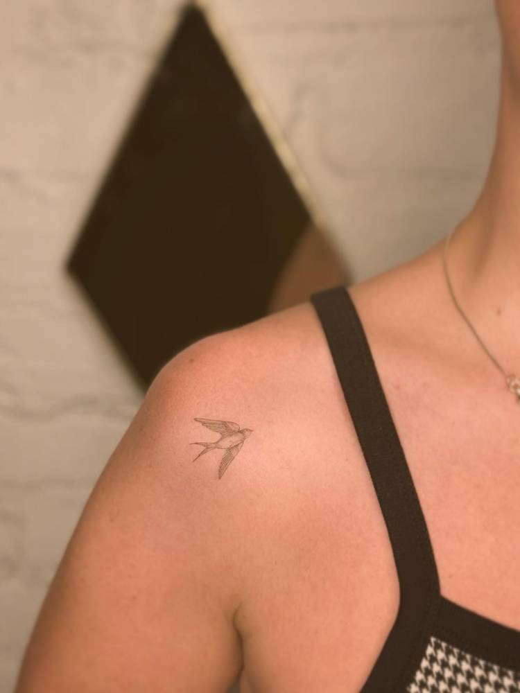 Little swallow in fine line style tattooed on the shoulder.