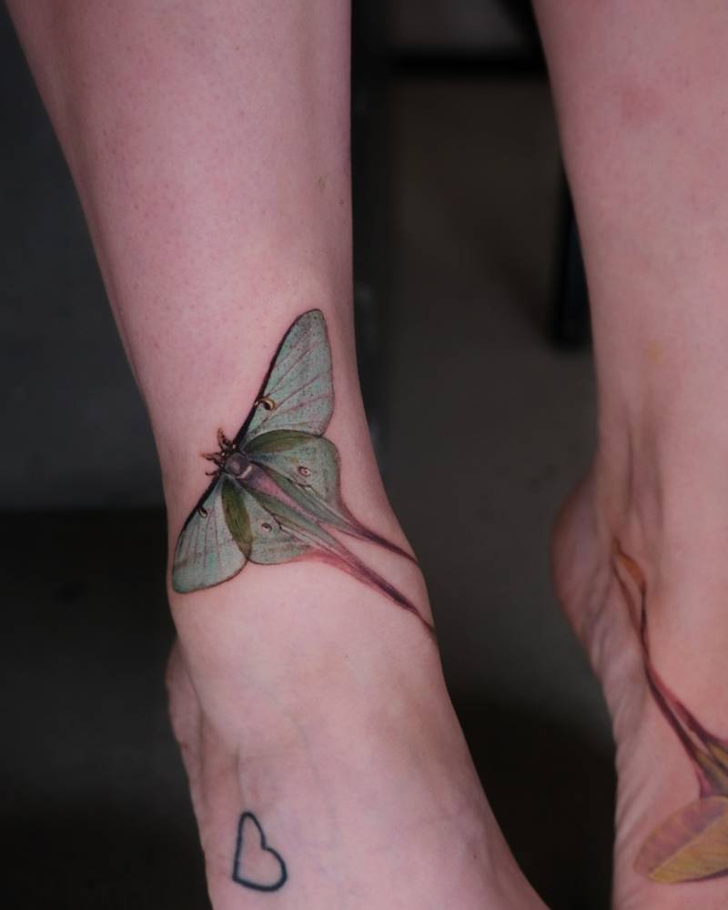 Green butterfly tattoo in watercolor style located on the ankle.