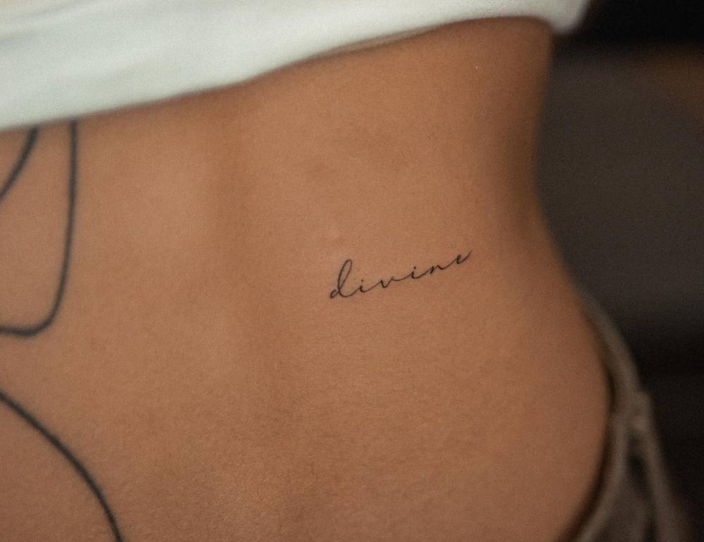 Tattoo of the word "divine" located on the lower back.