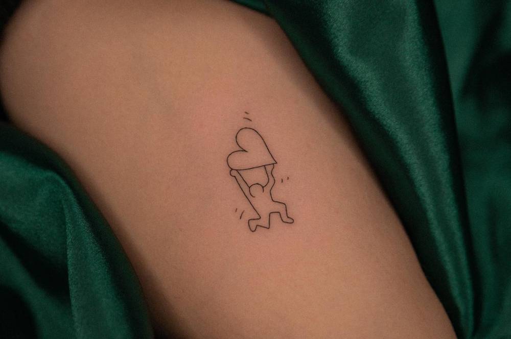 Minimalistic Keith Haring's artwork tattoo located on the inner arm.