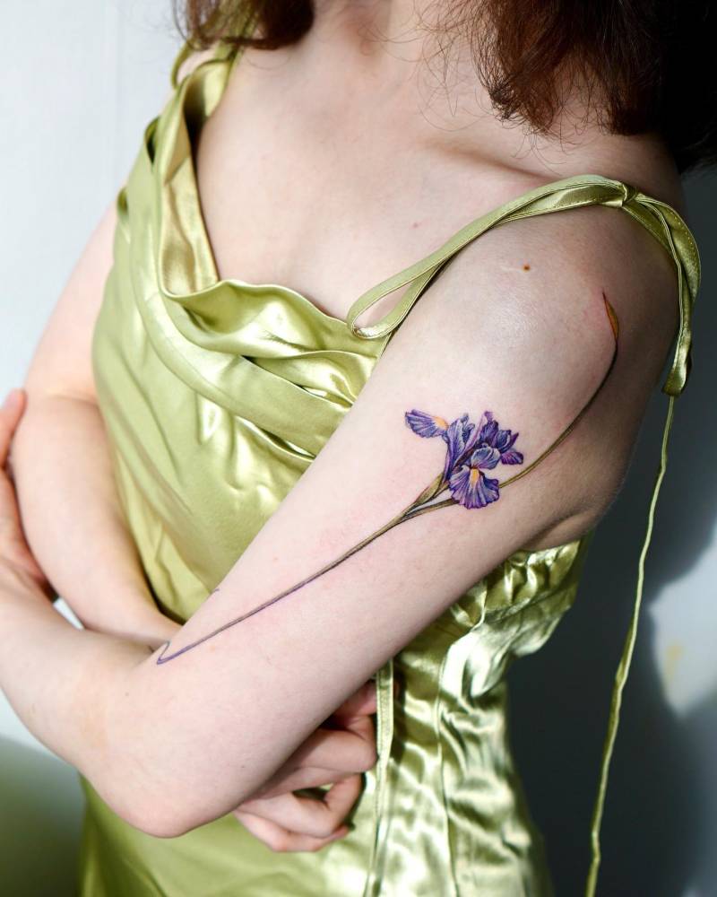 Watercolor style iris flower tattoo located on the upper arm.