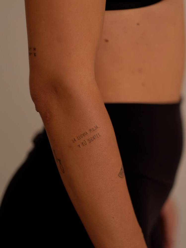 "La lluvia moja, y tú sientes" lettering tattoo placed on the forearm.