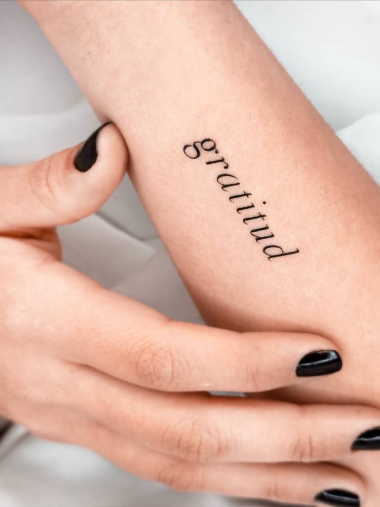 Serif font word "gratitud" tattooed on the wrist.