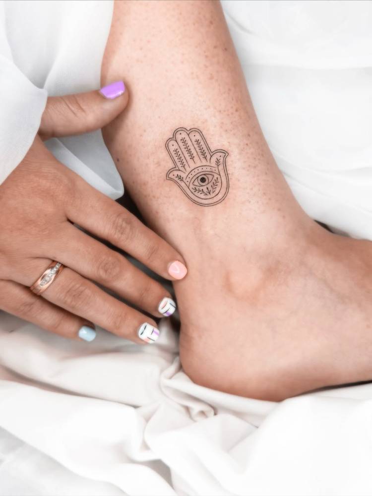 Hamsa tattoo located on the ankle, done in illustrative style.