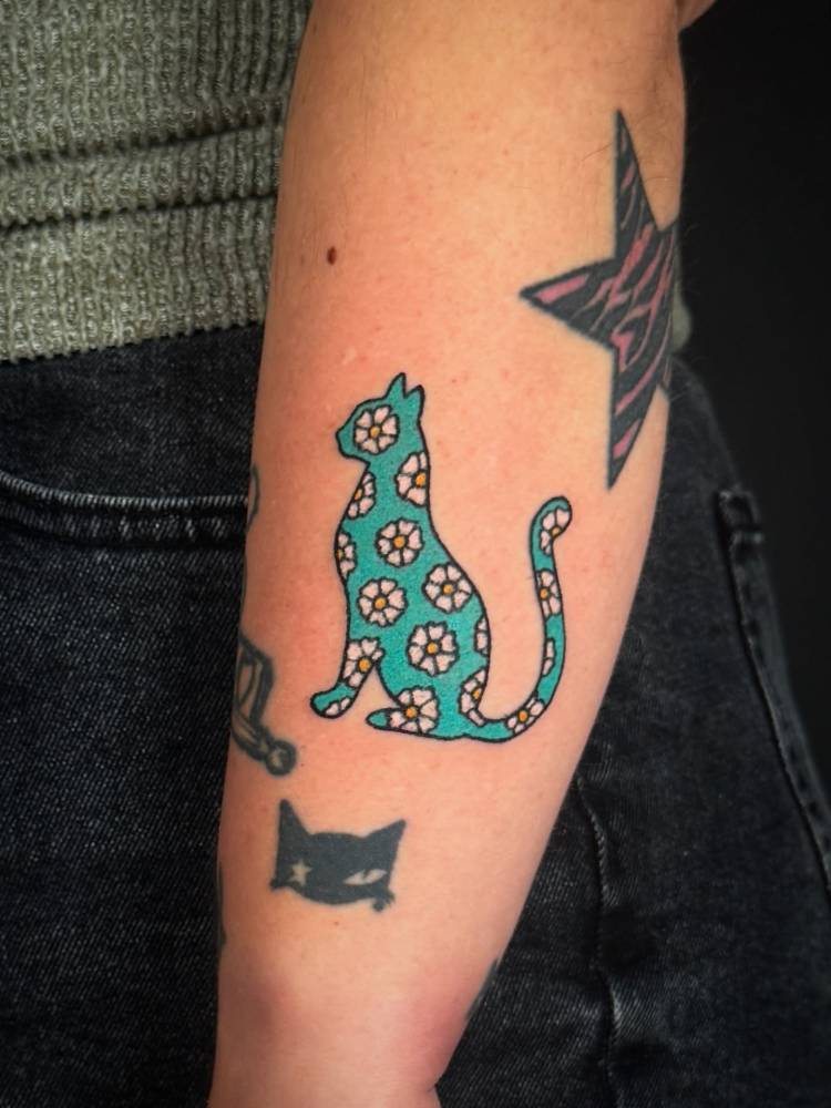 Floral cat tattoo in cartoon style located on the forearm.