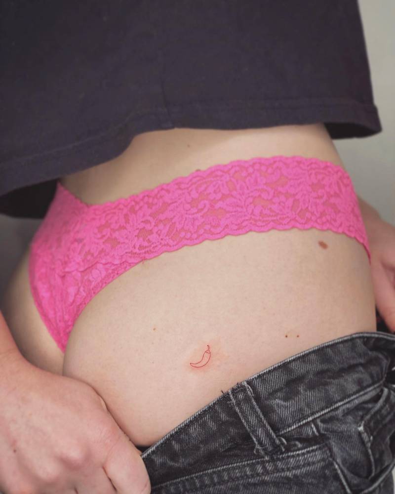 Tiny red chili pepper tattoo in minimalistic style placed on the butt cheek.