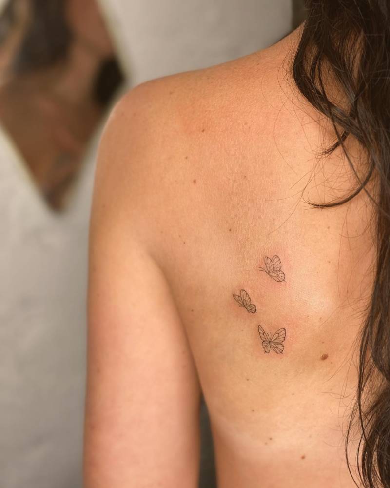 Little butterfly trio tattooed on the shoulder blade, fine line style.