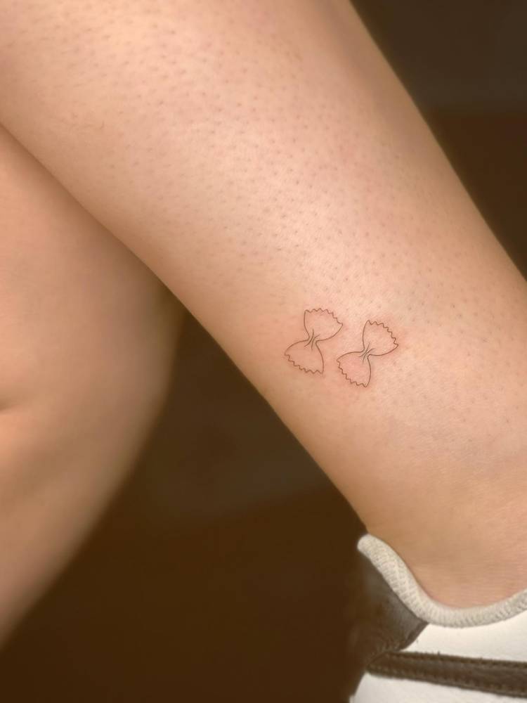 Fine line style farfalle pasta tattooed on the ankle, fine line style.