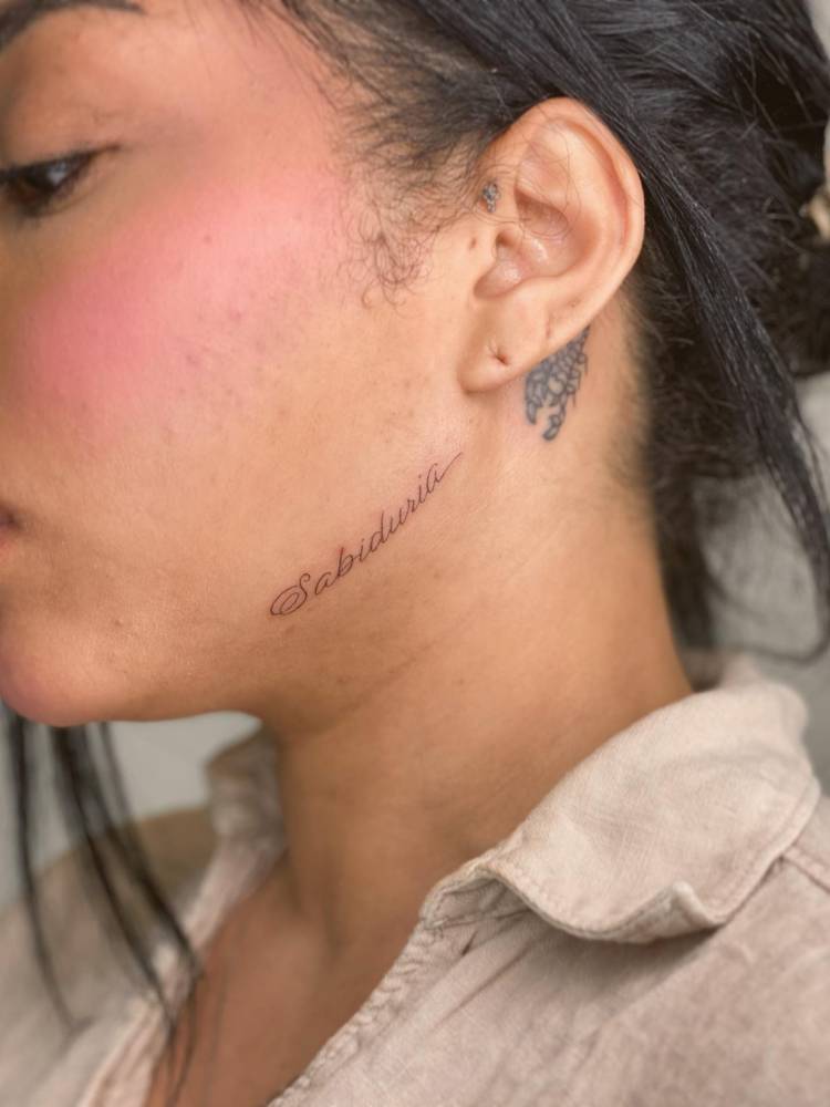 Handwritten font word "sabiduria" tattooed on the face.