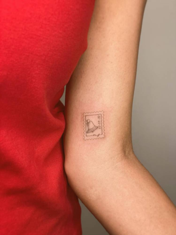 Bell stamp tattoo in fine line style placed on the inner arm.