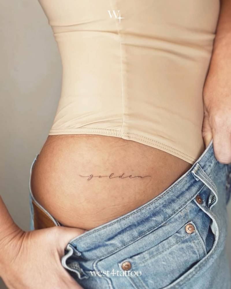 Lettering tattoo of the word "golden" in script font located on the hip.