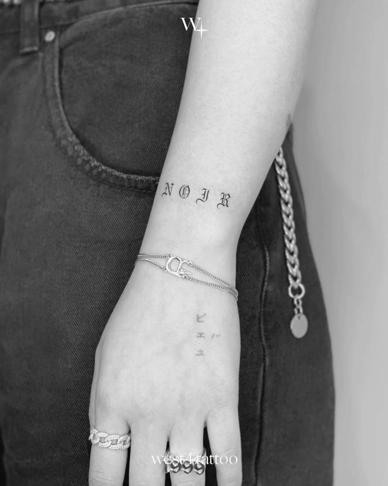 Gothic font word "noir" tattooed on the wrist.