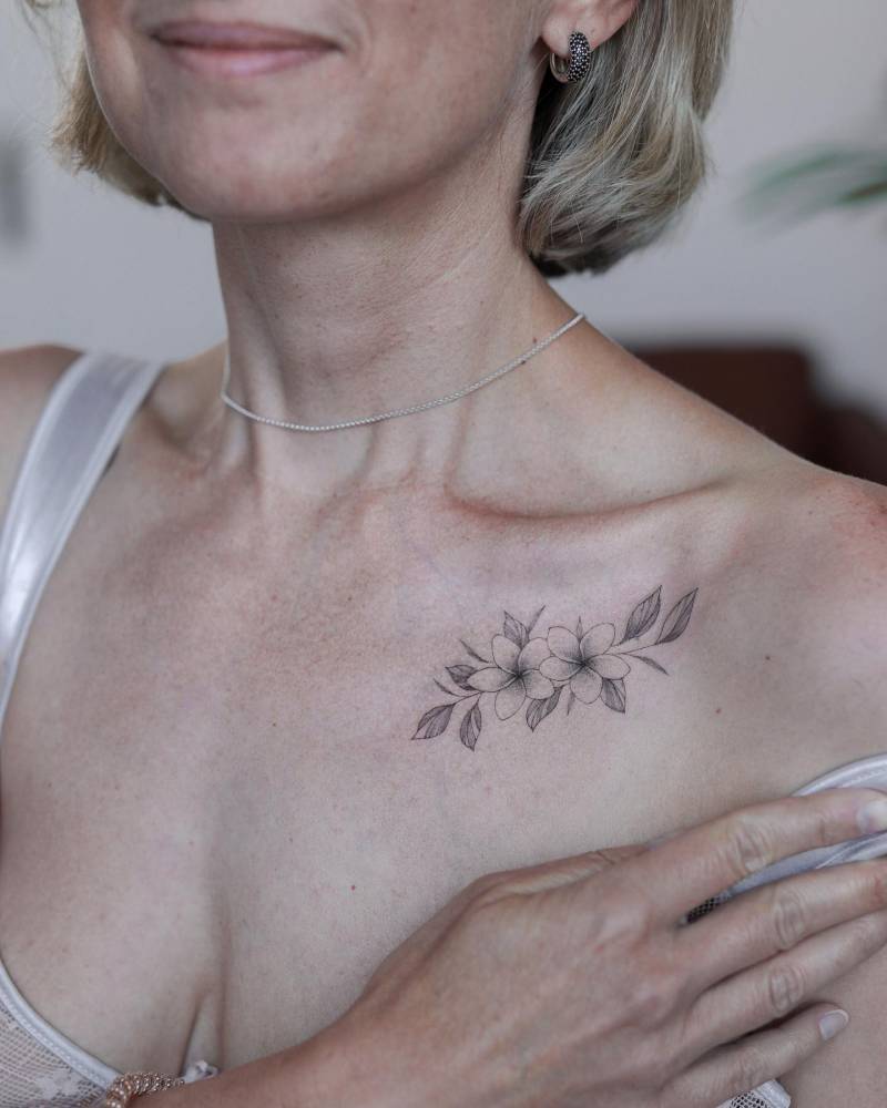 Plumeria tattoo placed on the collarbone, illustrative style.