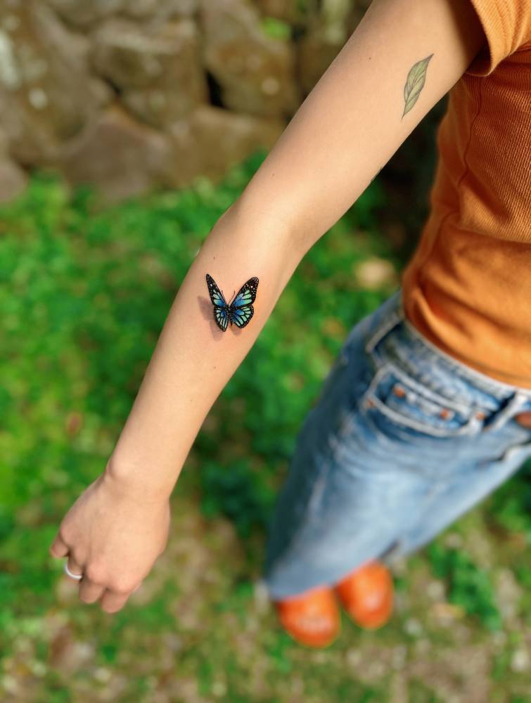 Micro-realistic style blue butterfly tattoo located on the forearm.