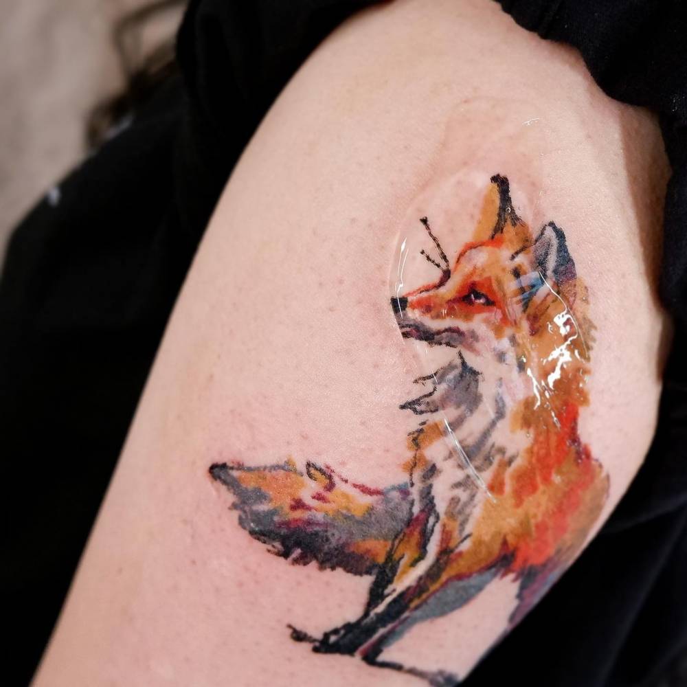 Watercolor style fox tattoo placed on the upper arm.